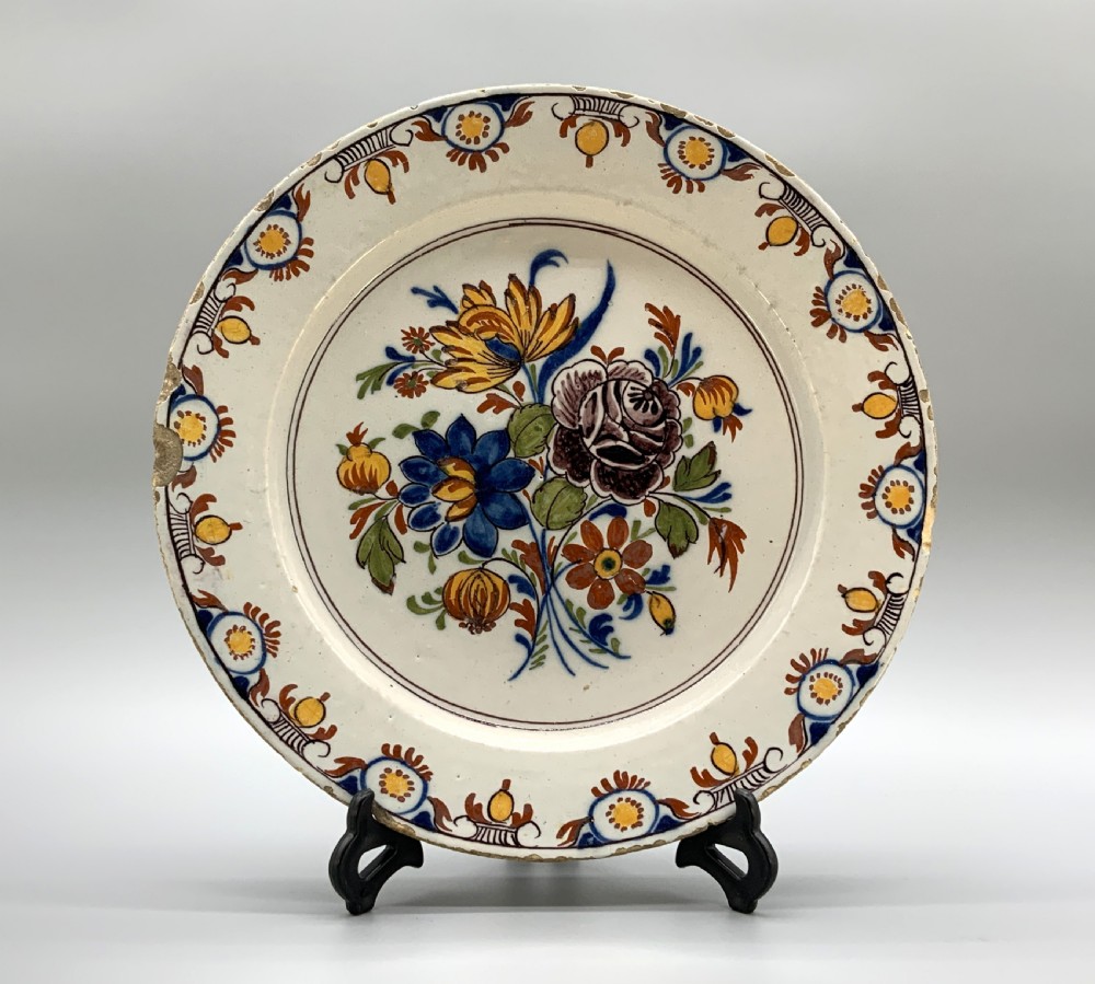 An 18th-century circular tin-glazed earthenware charger plate decorated with hand-painted floral motifs in manganese purple, cobalt blue, ochre yellow, and green. View XVIII