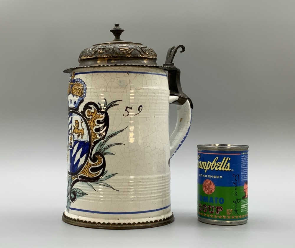 A 19th-century cream tin-glazed earthenware beer stein decorated with a hand-painted coat of arms and fitted with an embossed pewter lid. View II