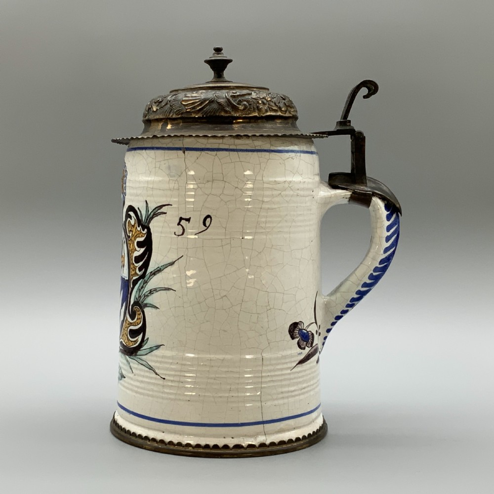 A 19th-century cream tin-glazed earthenware beer stein decorated with a hand-painted coat of arms and fitted with an embossed pewter lid. View V