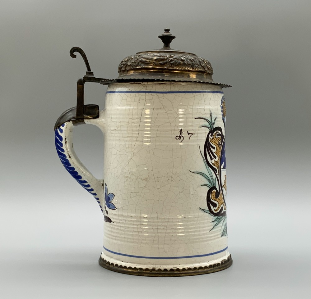A 19th-century cream tin-glazed earthenware beer stein decorated with a hand-painted coat of arms and fitted with an embossed pewter lid. View VI