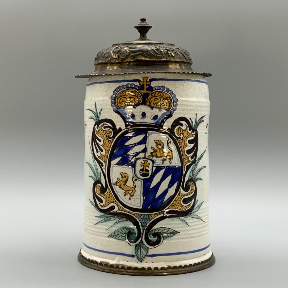 A 19th-century cream tin-glazed earthenware beer stein decorated with a hand-painted coat of arms and fitted with an embossed pewter lid. View VII