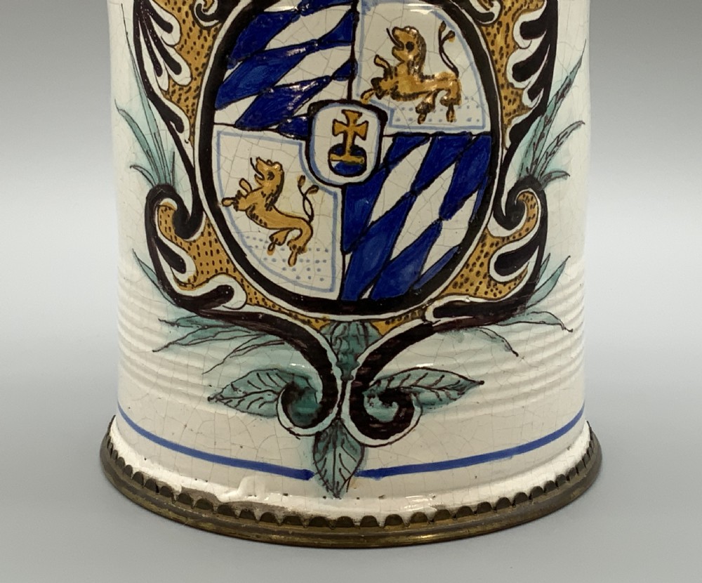 A 19th-century cream tin-glazed earthenware beer stein decorated with a hand-painted coat of arms and fitted with an embossed pewter lid. View IX