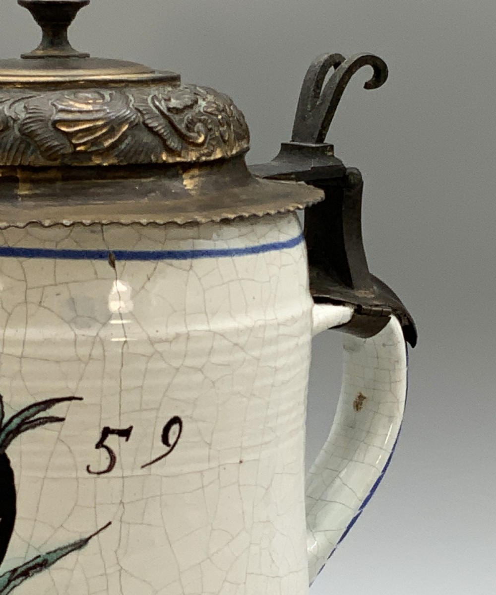 A 19th-century cream tin-glazed earthenware beer stein decorated with a hand-painted coat of arms and fitted with an embossed pewter lid. View XI