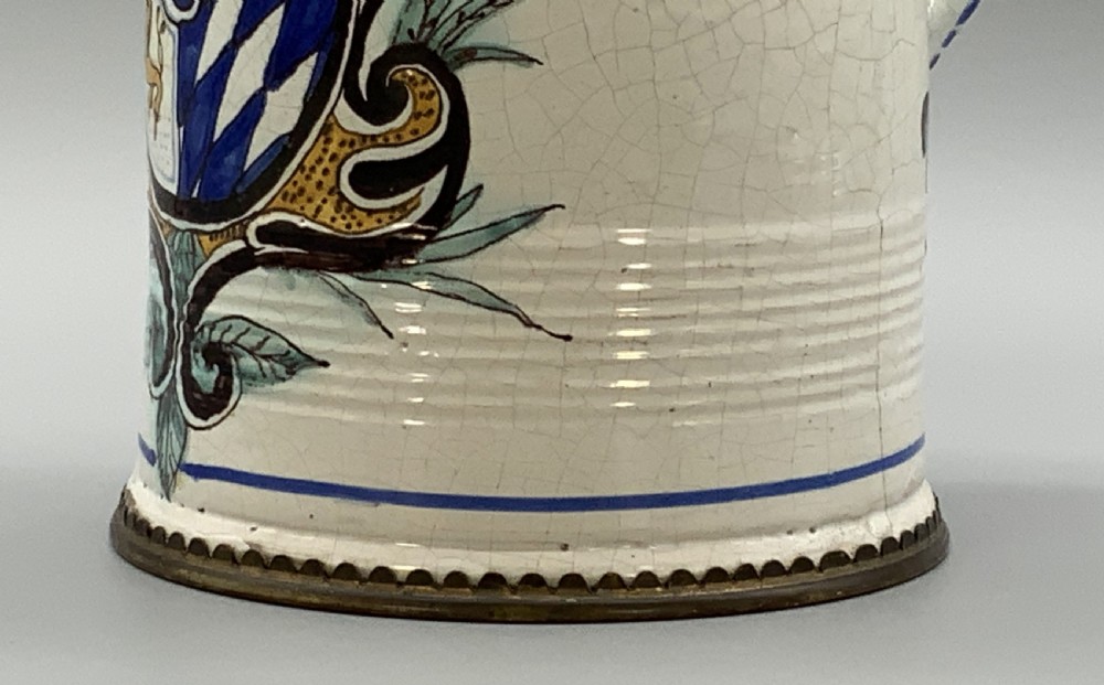 A 19th-century cream tin-glazed earthenware beer stein decorated with a hand-painted coat of arms and fitted with an embossed pewter lid. View XII