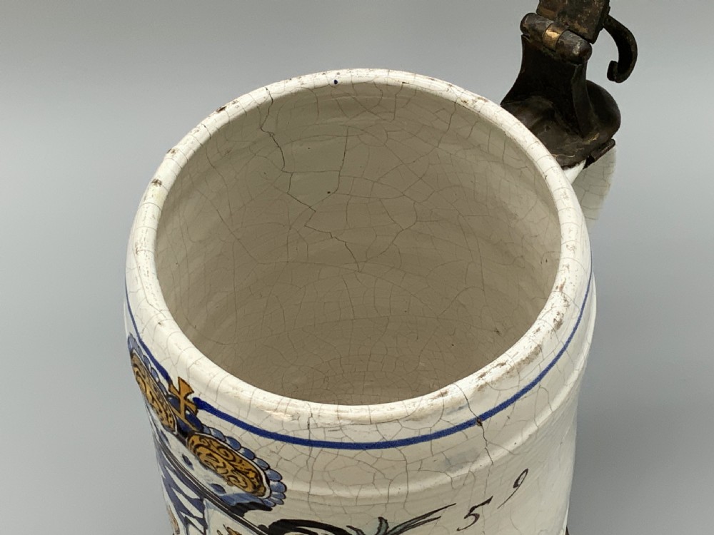 A 19th-century cream tin-glazed earthenware beer stein decorated with a hand-painted coat of arms and fitted with an embossed pewter lid. View XIII