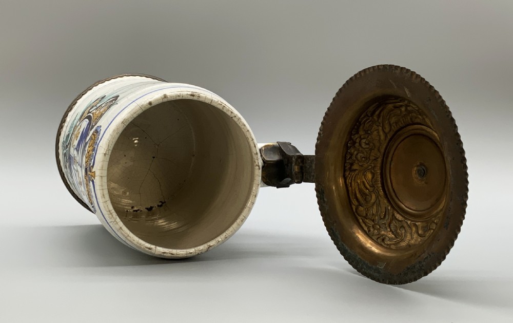 A 19th-century cream tin-glazed earthenware beer stein decorated with a hand-painted coat of arms and fitted with an embossed pewter lid. View XIV