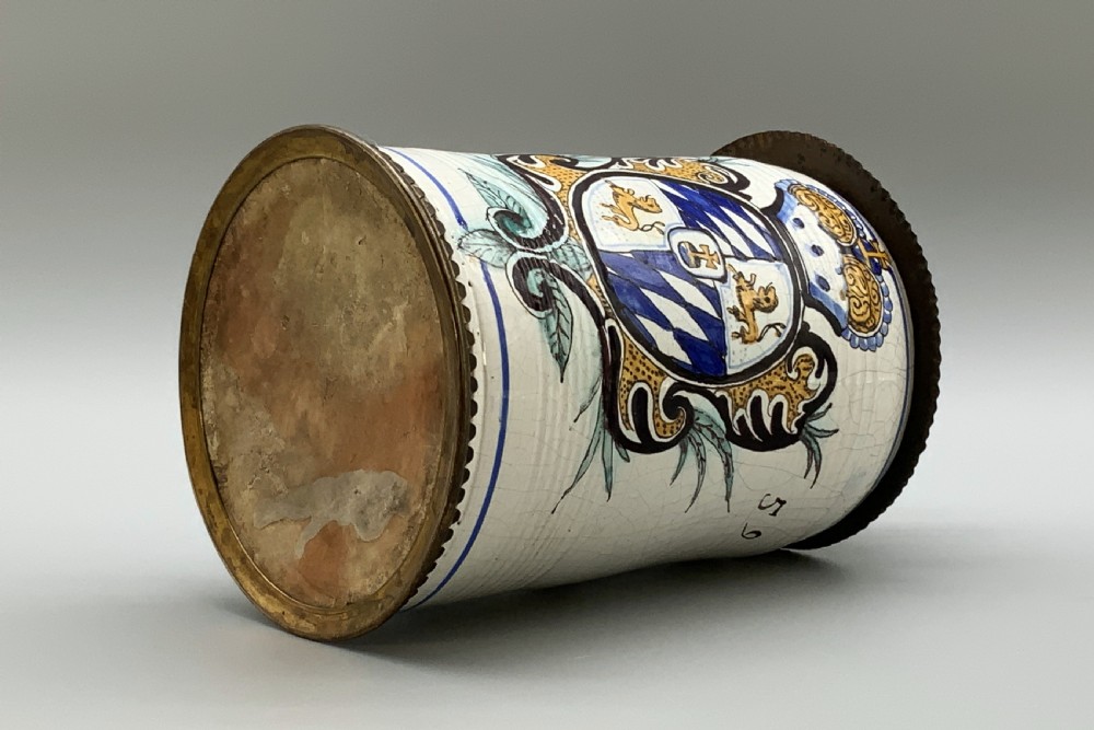 A 19th-century cream tin-glazed earthenware beer stein decorated with a hand-painted coat of arms and fitted with an embossed pewter lid. View XVI
