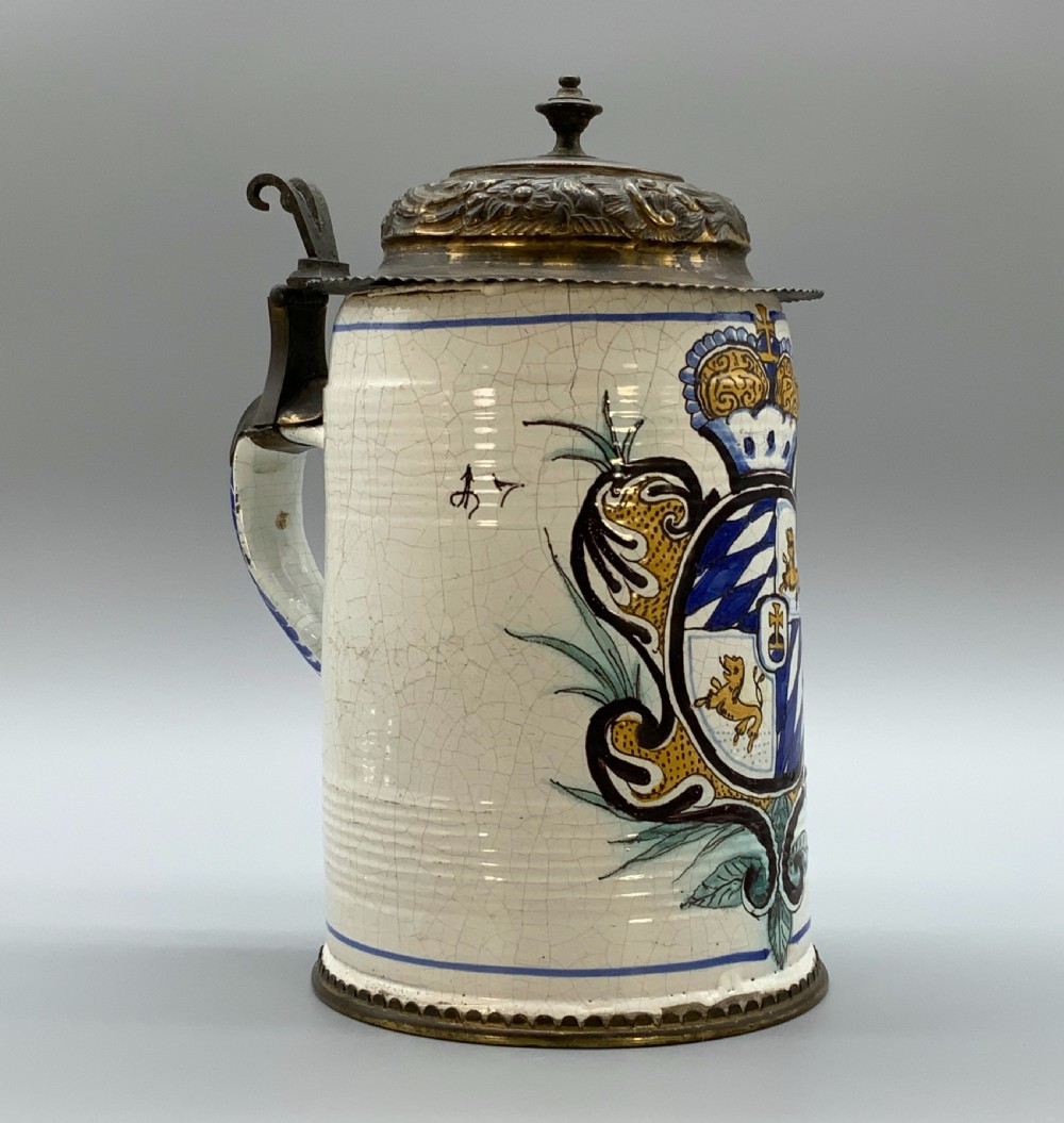 A 19th-century cream tin-glazed earthenware beer stein decorated with a hand-painted coat of arms and fitted with an embossed pewter lid. View XVII