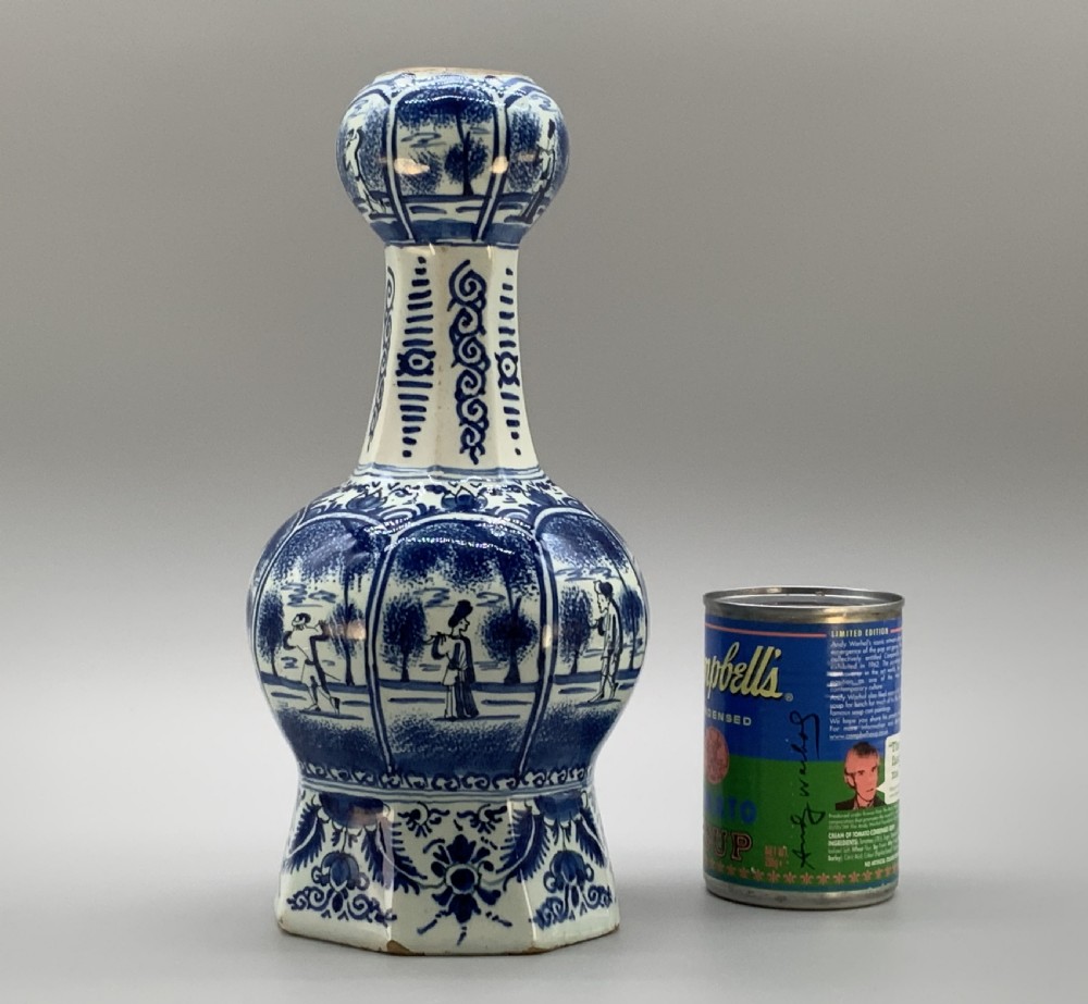 A tall, octagonal blue and white tin-glazed earthenware vase featuring a garlic bulb neck and hand-painted Chinoiserie scenes within arched panels. View II