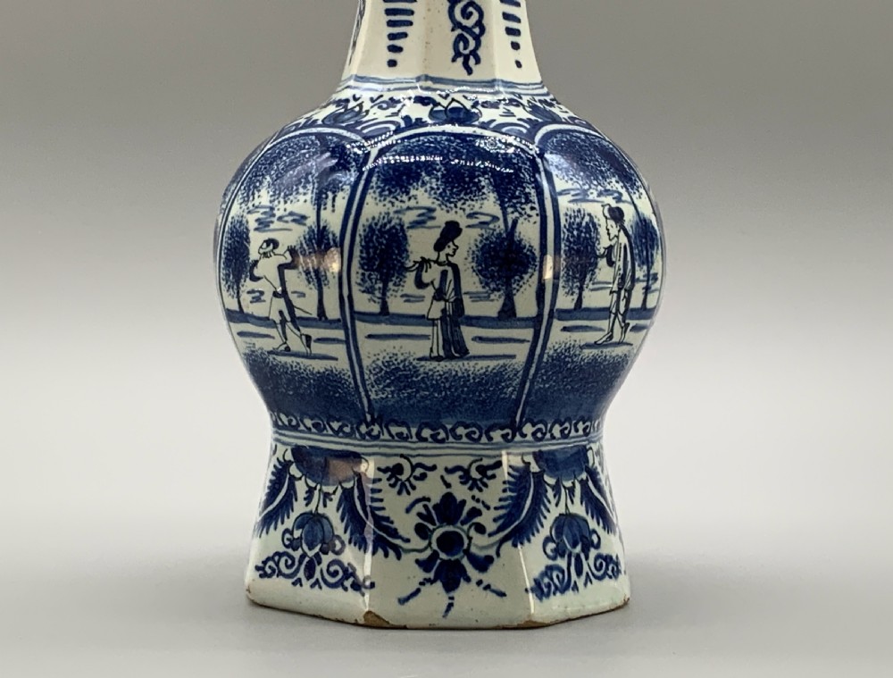 A tall, octagonal blue and white tin-glazed earthenware vase featuring a garlic bulb neck and hand-painted Chinoiserie scenes within arched panels. View III
