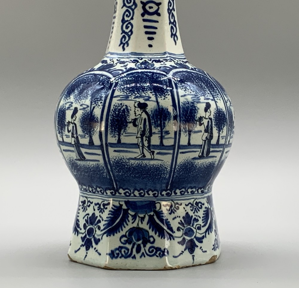 A tall, octagonal blue and white tin-glazed earthenware vase featuring a garlic bulb neck and hand-painted Chinoiserie scenes within arched panels. View VI
