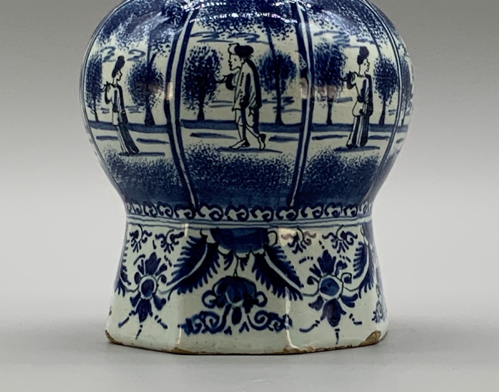 A tall, octagonal blue and white tin-glazed earthenware vase featuring a garlic bulb neck and hand-painted Chinoiserie scenes within arched panels. View VIII