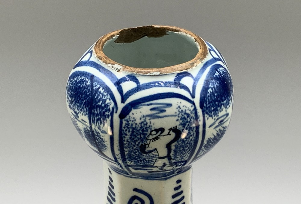 A tall, octagonal blue and white tin-glazed earthenware vase featuring a garlic bulb neck and hand-painted Chinoiserie scenes within arched panels. View X