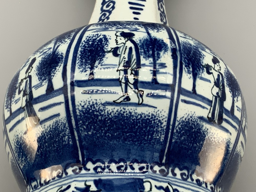 A tall, octagonal blue and white tin-glazed earthenware vase featuring a garlic bulb neck and hand-painted Chinoiserie scenes within arched panels. View XIX
