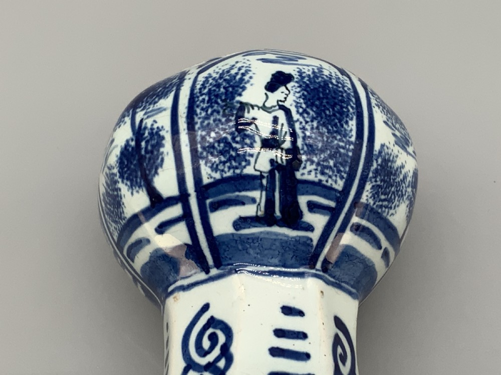 A tall, octagonal blue and white tin-glazed earthenware vase featuring a garlic bulb neck and hand-painted Chinoiserie scenes within arched panels. View XX