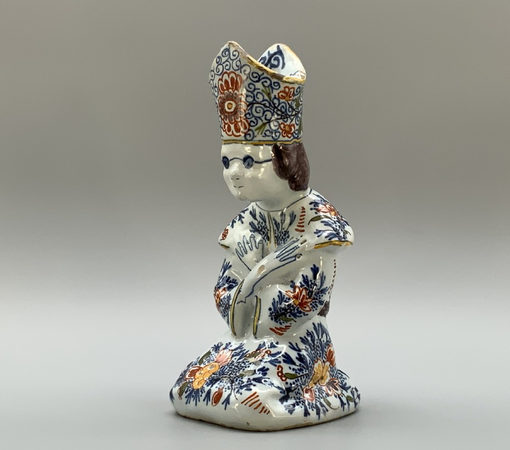 An 18th-century Dutch Delftware ceramic candlestick formed as a kneeling bishop in patterned robes and a mitre decorated with polychrome glazes.
