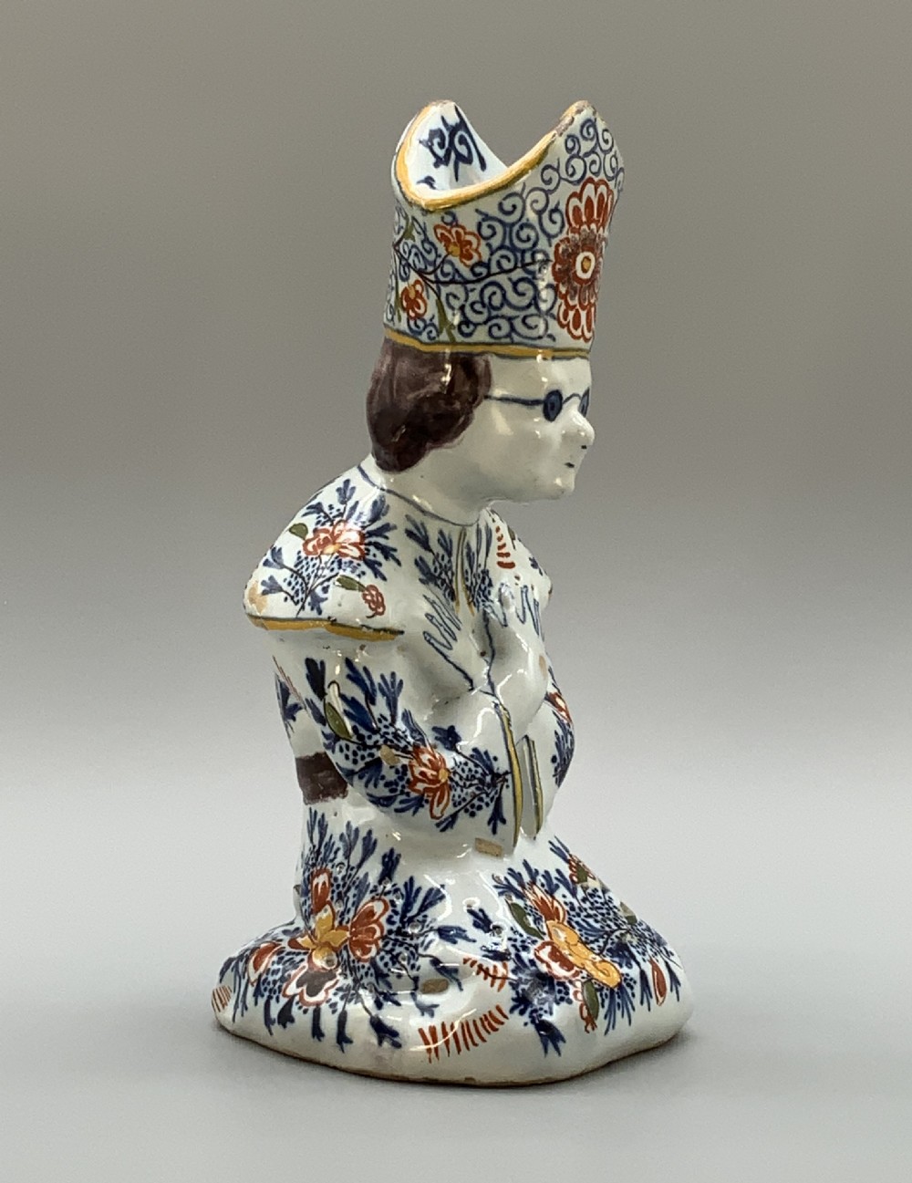 An 18th-century Dutch Delftware ceramic candlestick formed as a kneeling bishop in patterned robes and a mitre decorated with polychrome glazes. View III
