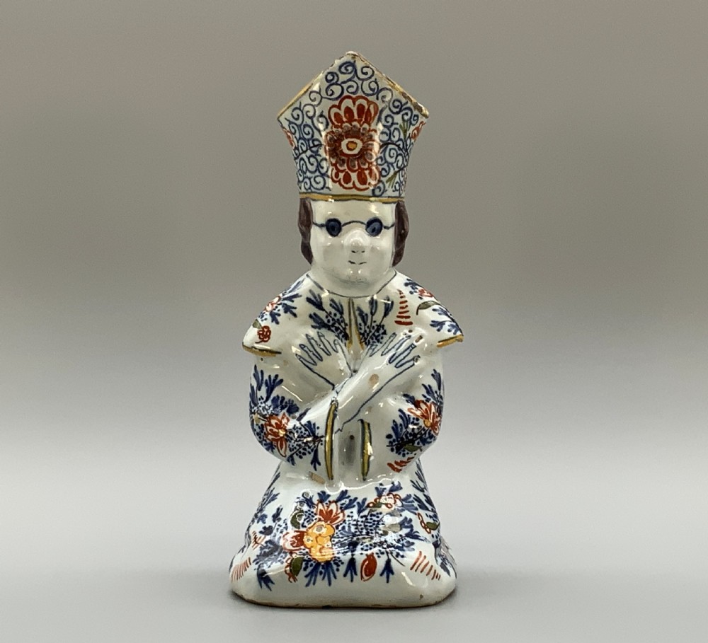 An 18th-century Dutch Delftware ceramic candlestick formed as a kneeling bishop in patterned robes and a mitre decorated with polychrome glazes. View V
