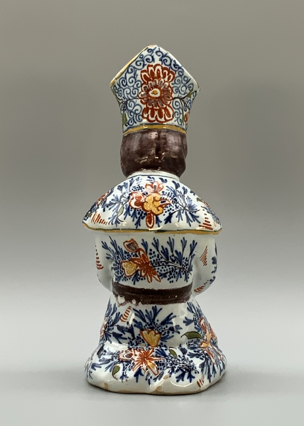 An 18th-century Dutch Delftware ceramic candlestick formed as a kneeling bishop in patterned robes and a mitre decorated with polychrome glazes. View VIII