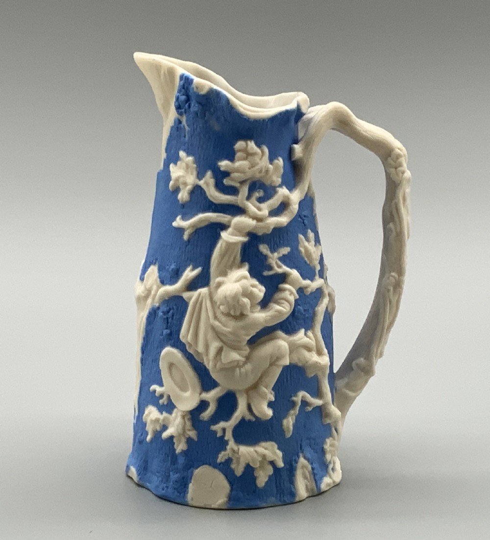 A Victorian blue and white Parian ware jug featuring a textured cobalt blue ground with raised white relief figures climbing a tree and a moulded branch handle.
