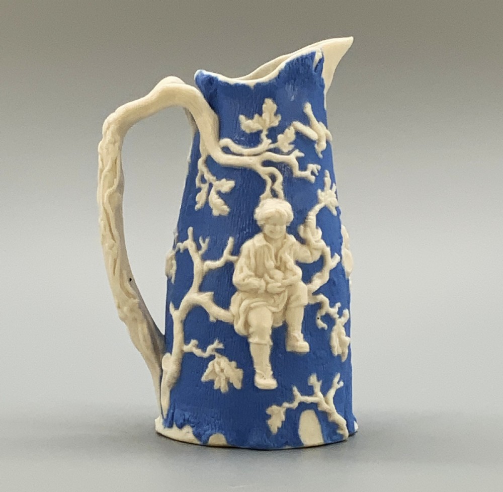 A Victorian blue and white Parian ware jug featuring a textured cobalt blue ground with raised white relief figures climbing a tree and a moulded branch handle. View VIII