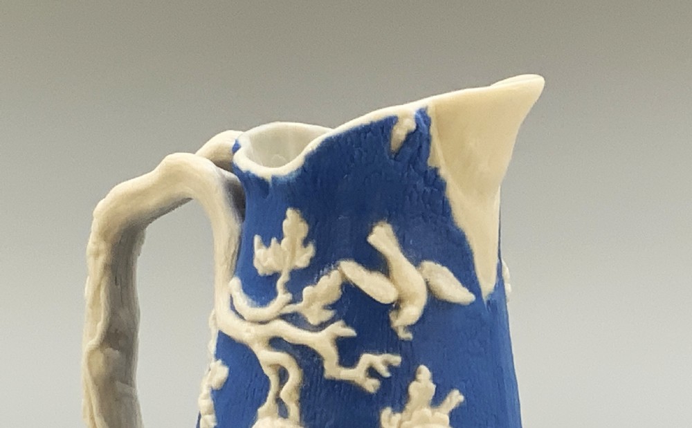 A Victorian blue and white Parian ware jug featuring a textured cobalt blue ground with raised white relief figures climbing a tree and a moulded branch handle. View IX