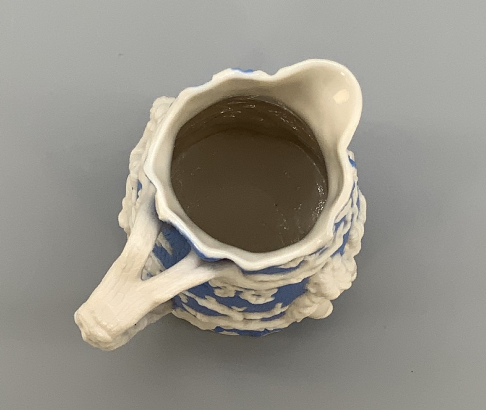 A Victorian blue and white Parian ware jug featuring a textured cobalt blue ground with raised white relief figures climbing a tree and a moulded branch handle. View XV