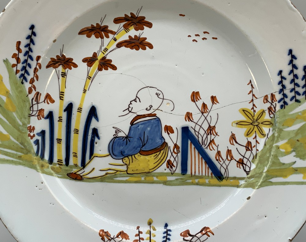 An eighteenth-century circular tin-glazed earthenware charger plate featuring a hand-painted polychrome Chinoiserie scene of a seated figure among bamboo and foliage. View III