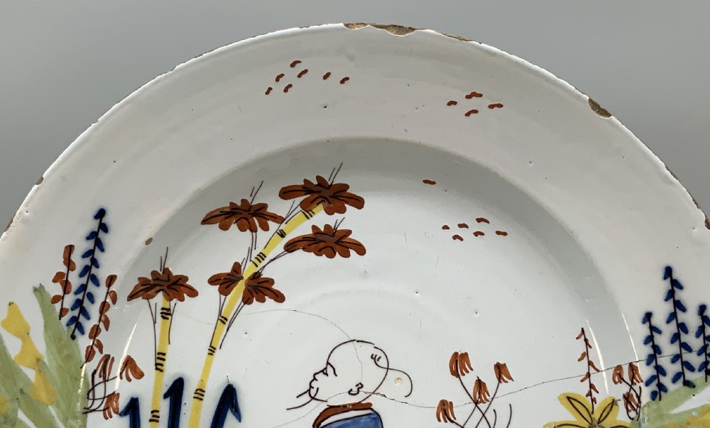 An eighteenth-century circular tin-glazed earthenware charger plate featuring a hand-painted polychrome Chinoiserie scene of a seated figure among bamboo and foliage. View V