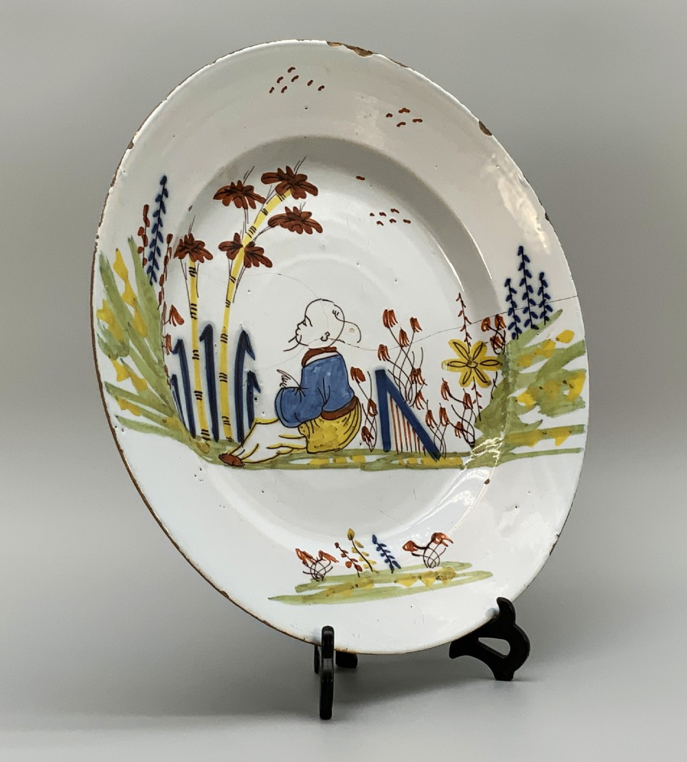 An eighteenth-century circular tin-glazed earthenware charger plate featuring a hand-painted polychrome Chinoiserie scene of a seated figure among bamboo and foliage. View XII