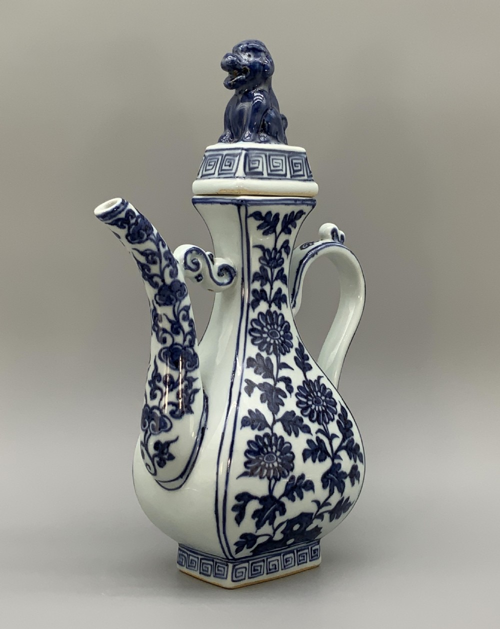 A blue and white porcelain ewer decorated with hand-painted floral foliage, featuring a high curved handle, slender curved spout, and a cover with a Foo dog finial. View VII
