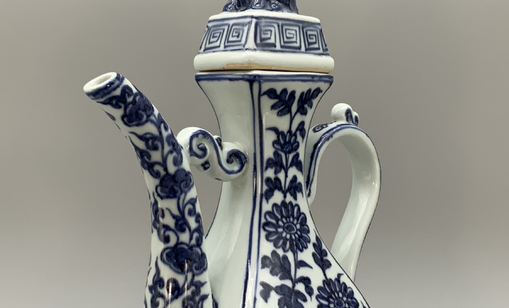 A blue and white porcelain ewer decorated with hand-painted floral foliage, featuring a high curved handle, slender curved spout, and a cover with a Foo dog finial. View XI