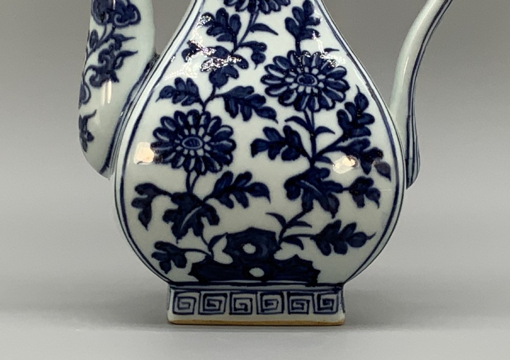 A blue and white porcelain ewer decorated with hand-painted floral foliage, featuring a high curved handle, slender curved spout, and a cover with a Foo dog finial. View XVI