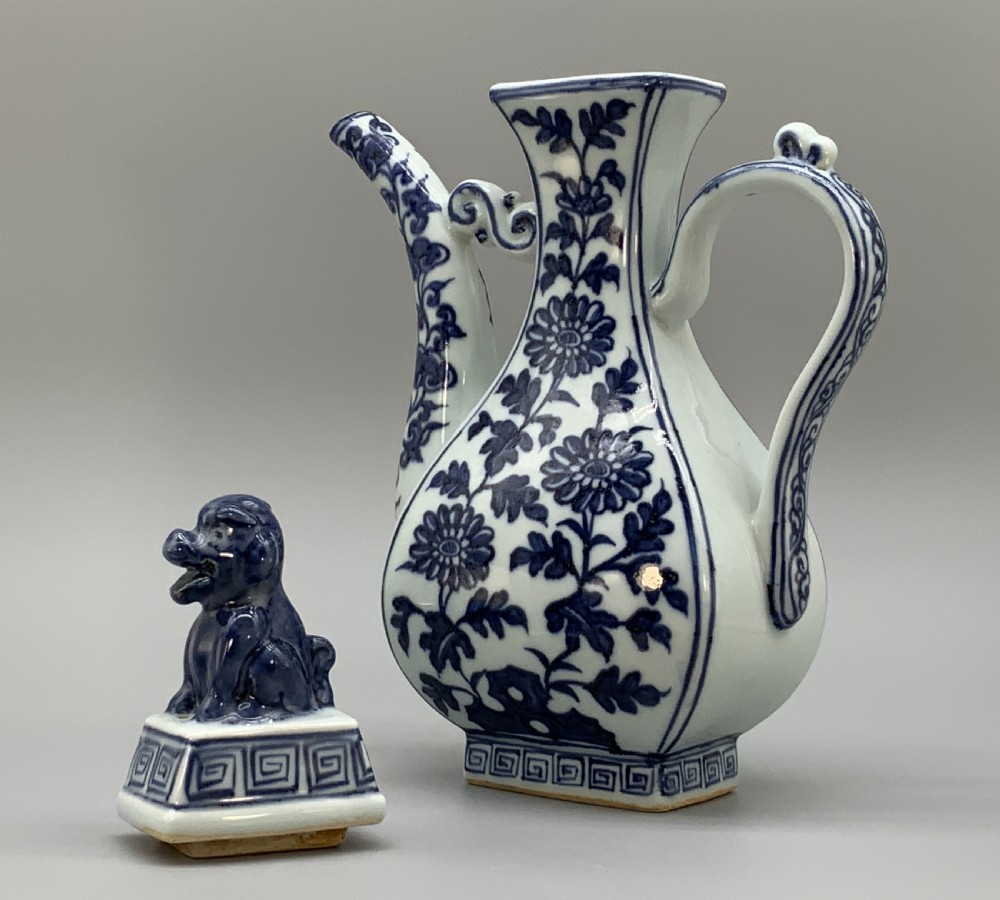 A blue and white porcelain ewer decorated with hand-painted floral foliage, featuring a high curved handle, slender curved spout, and a cover with a Foo dog finial. View XVII
