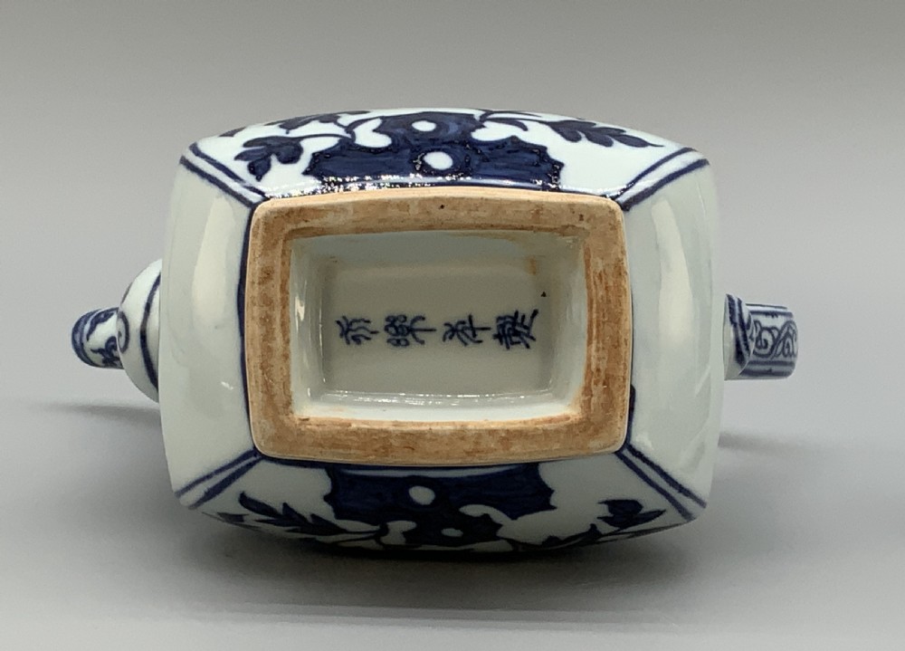 A blue and white porcelain ewer decorated with hand-painted floral foliage, featuring a high curved handle, slender curved spout, and a cover with a Foo dog finial. View XIX