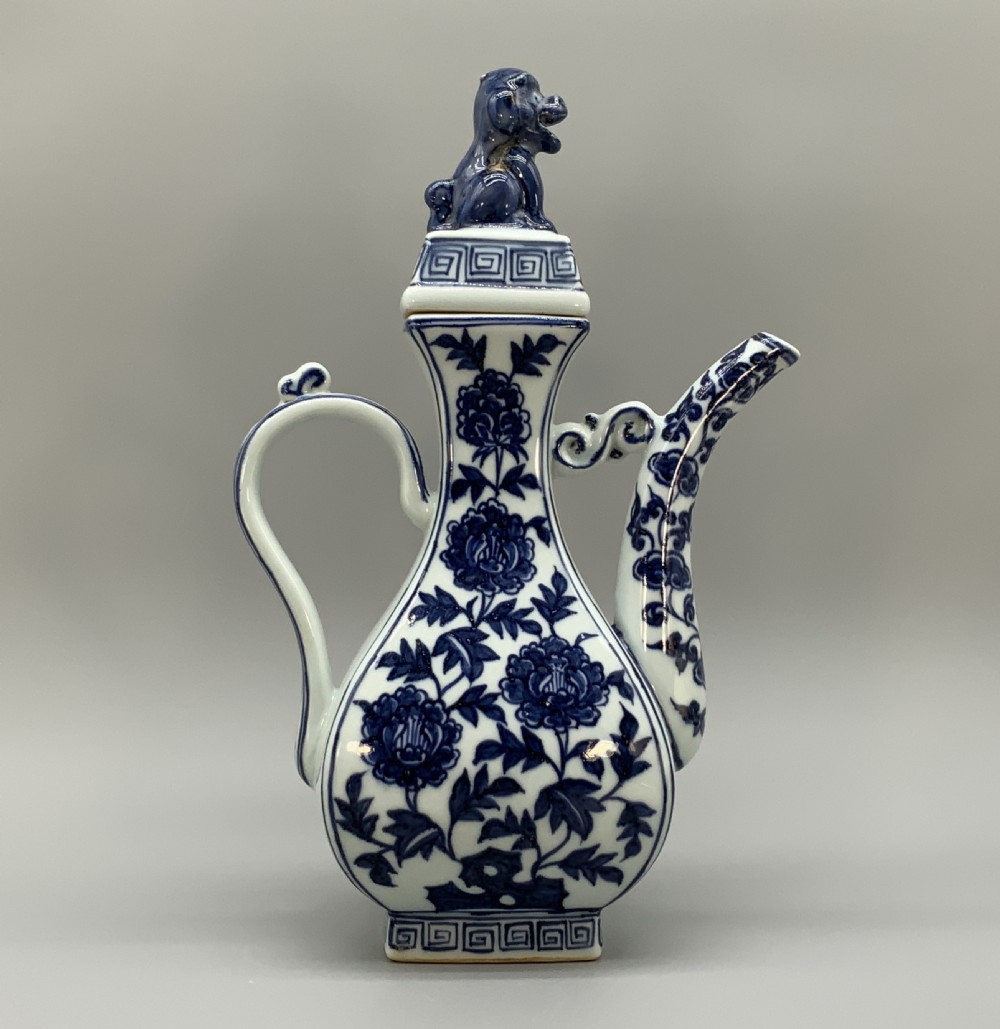 A blue and white porcelain ewer decorated with hand-painted floral foliage, featuring a high curved handle, slender curved spout, and a cover with a Foo dog finial. View XX