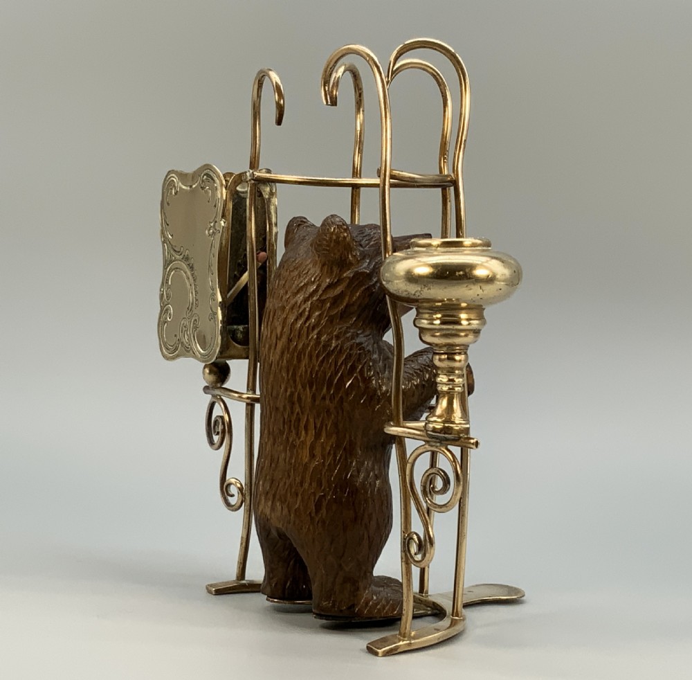 A 19th-century carved wooden bear standing upright inside a brass wire cage, attached to a brass candlestick holder on the left and an engraved brass vesta case on the right. View VI