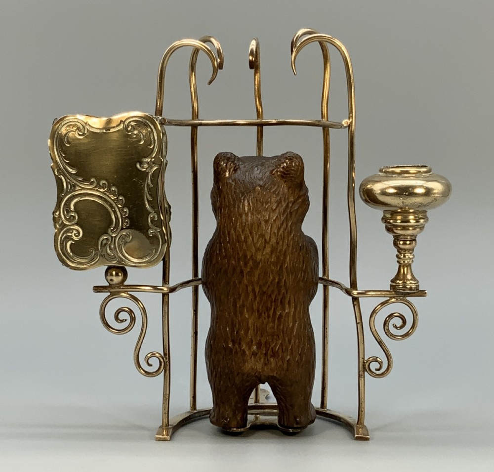 A 19th-century carved wooden bear standing upright inside a brass wire cage, attached to a brass candlestick holder on the left and an engraved brass vesta case on the right. View VII