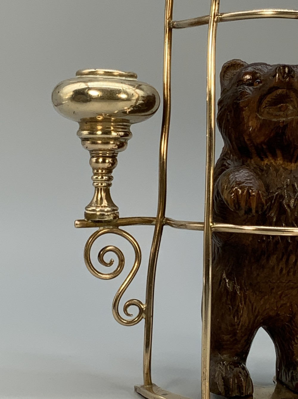 A 19th-century carved wooden bear standing upright inside a brass wire cage, attached to a brass candlestick holder on the left and an engraved brass vesta case on the right. View X