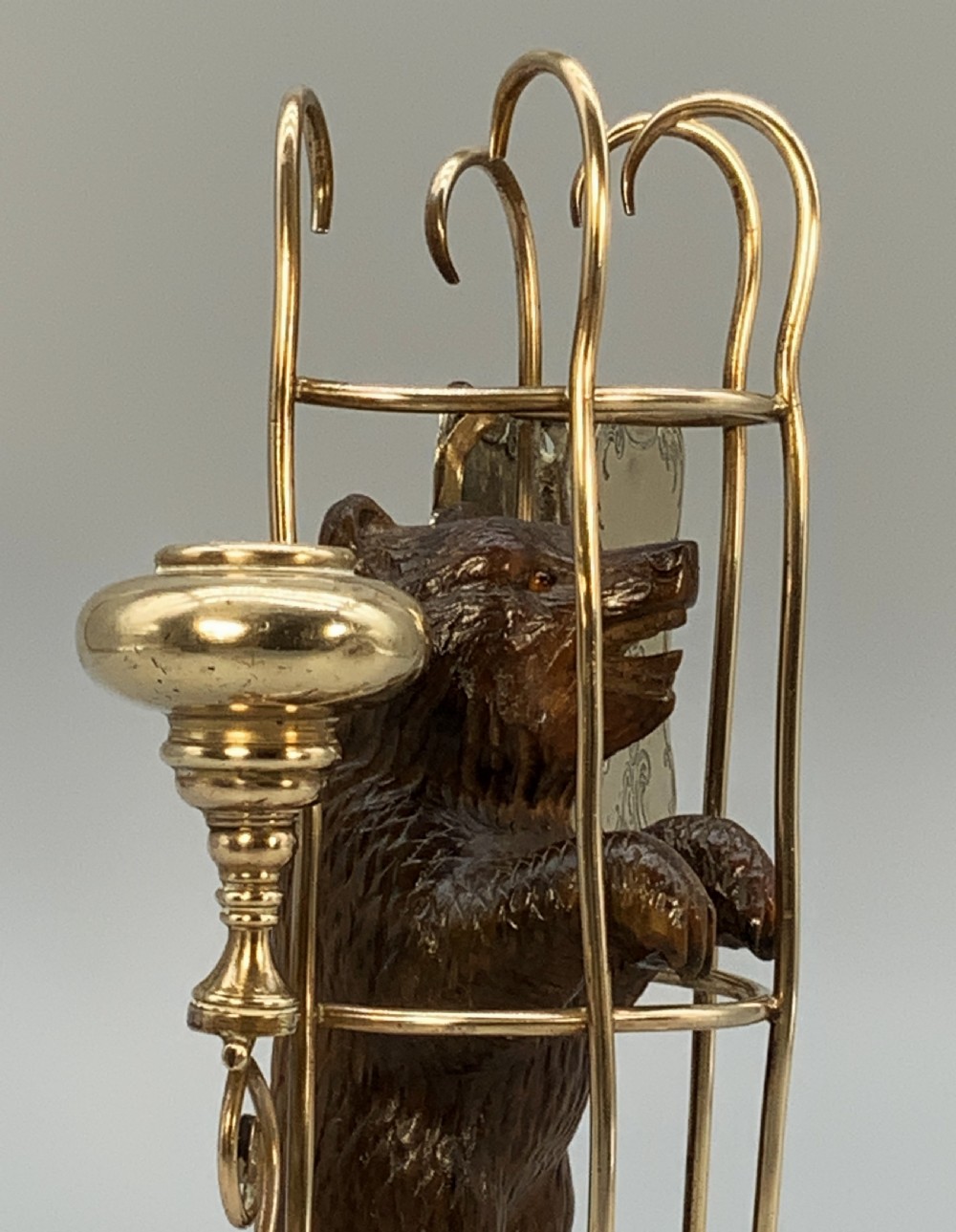 A 19th-century carved wooden bear standing upright inside a brass wire cage, attached to a brass candlestick holder on the left and an engraved brass vesta case on the right. View XII
