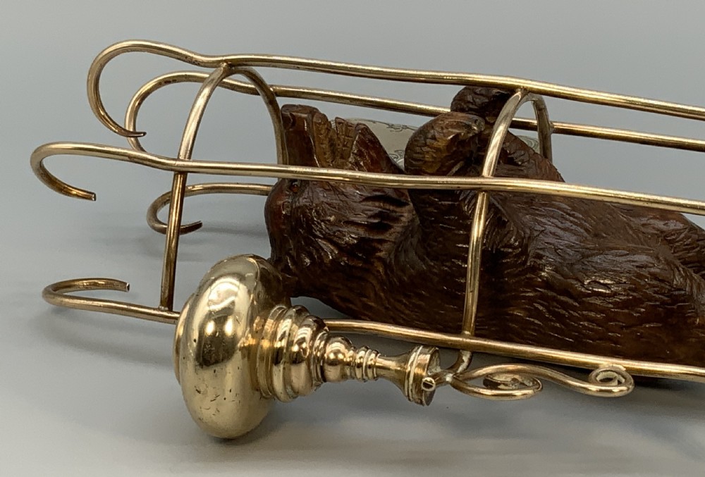 A 19th-century carved wooden bear standing upright inside a brass wire cage, attached to a brass candlestick holder on the left and an engraved brass vesta case on the right. View XVII