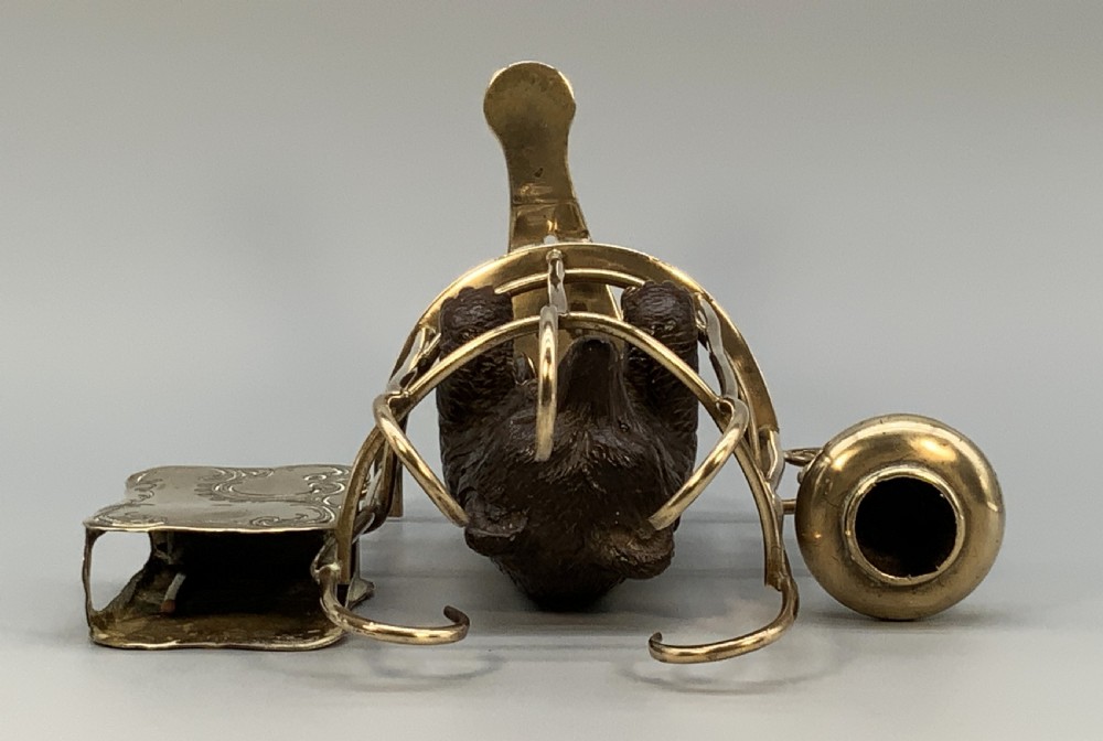 A 19th-century carved wooden bear standing upright inside a brass wire cage, attached to a brass candlestick holder on the left and an engraved brass vesta case on the right. View XVIII