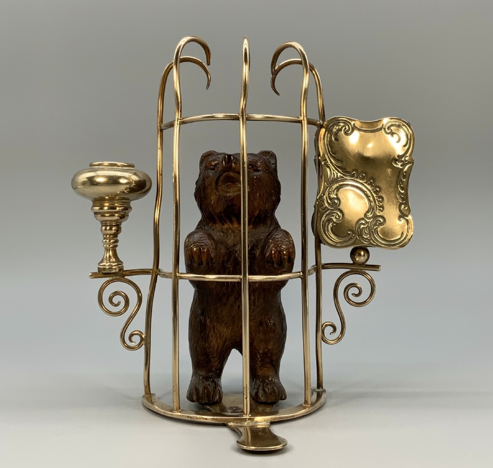 A 19th-century carved wooden bear standing upright inside a brass wire cage, attached to a brass candlestick holder on the left and an engraved brass vesta case on the right. View XIX