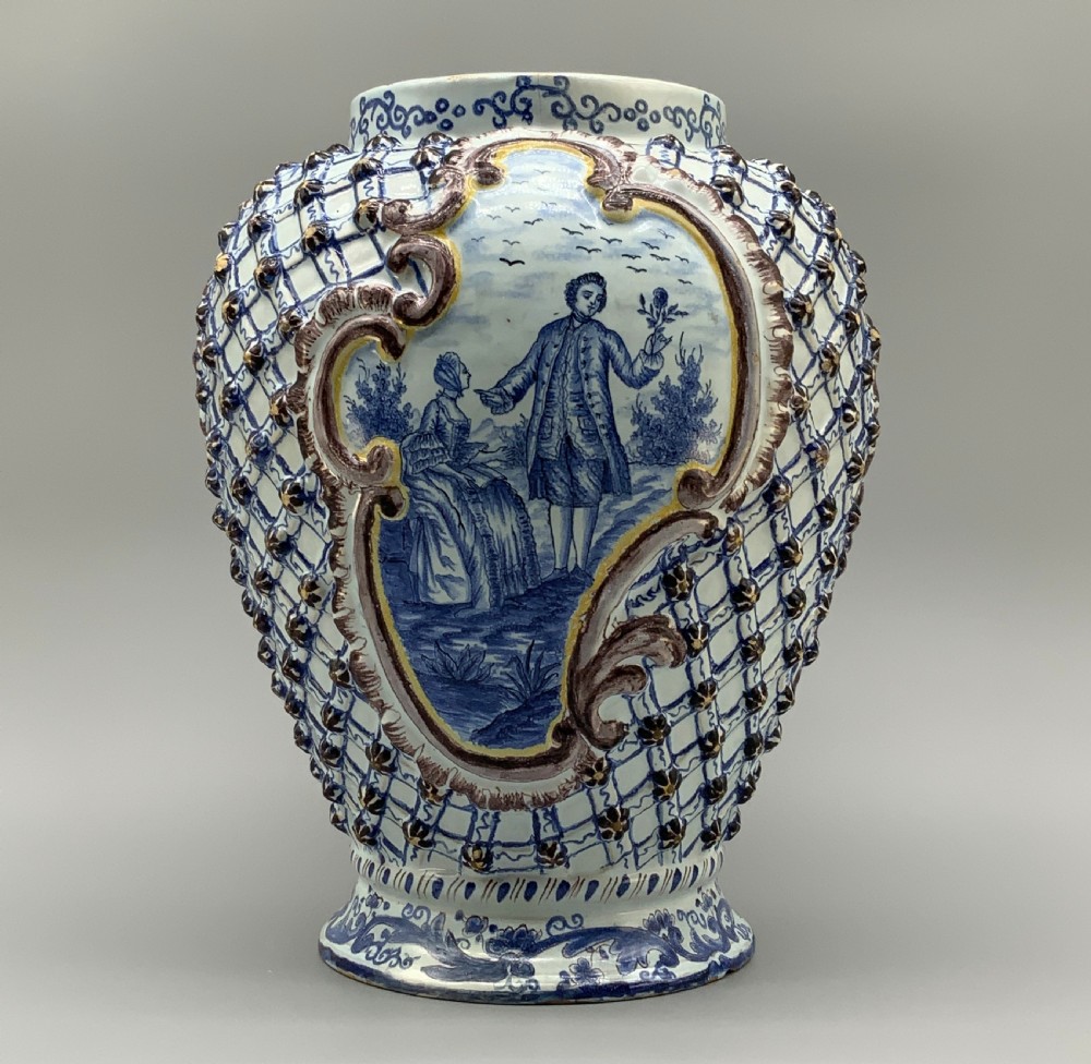 A large 19th-century French faience baluster vase decorated with blue and white glazes, featuring a central Rococo cartouche with figures in a landscape surrounded by moulded lattice work and manganese detailing. View II