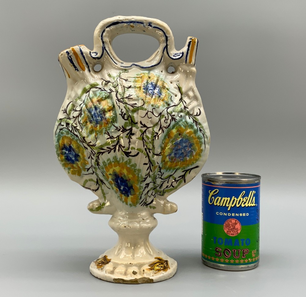 An 18th-century Italian polychrome majolica pilgrim flask formed as a scallop shell with an overhead handle, side loops, and hand-painted floral motifs in blue, yellow, and green over a cream glazed surface. View II
