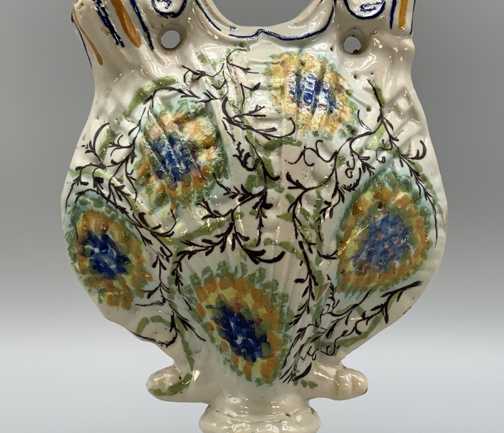 An 18th-century Italian polychrome majolica pilgrim flask formed as a scallop shell with an overhead handle, side loops, and hand-painted floral motifs in blue, yellow, and green over a cream glazed surface. View IX