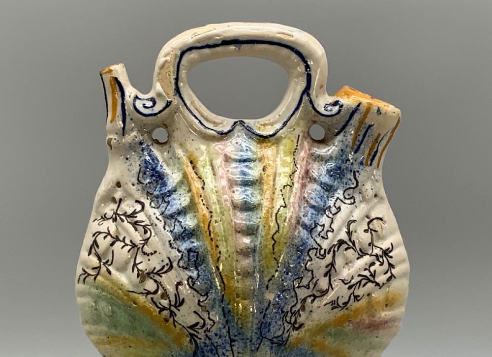 An 18th-century Italian polychrome majolica pilgrim flask formed as a scallop shell with an overhead handle, side loops, and hand-painted floral motifs in blue, yellow, and green over a cream glazed surface. View XII