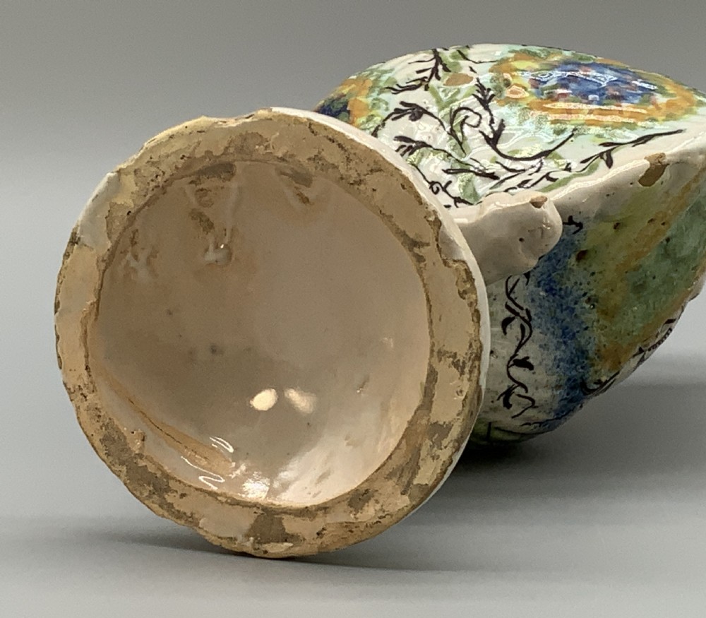 An 18th-century Italian polychrome majolica pilgrim flask formed as a scallop shell with an overhead handle, side loops, and hand-painted floral motifs in blue, yellow, and green over a cream glazed surface. View XVI
