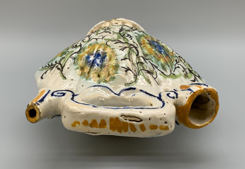 An 18th-century Italian polychrome majolica pilgrim flask formed as a scallop shell with an overhead handle, side loops, and hand-painted floral motifs in blue, yellow, and green over a cream glazed surface. View XVIII