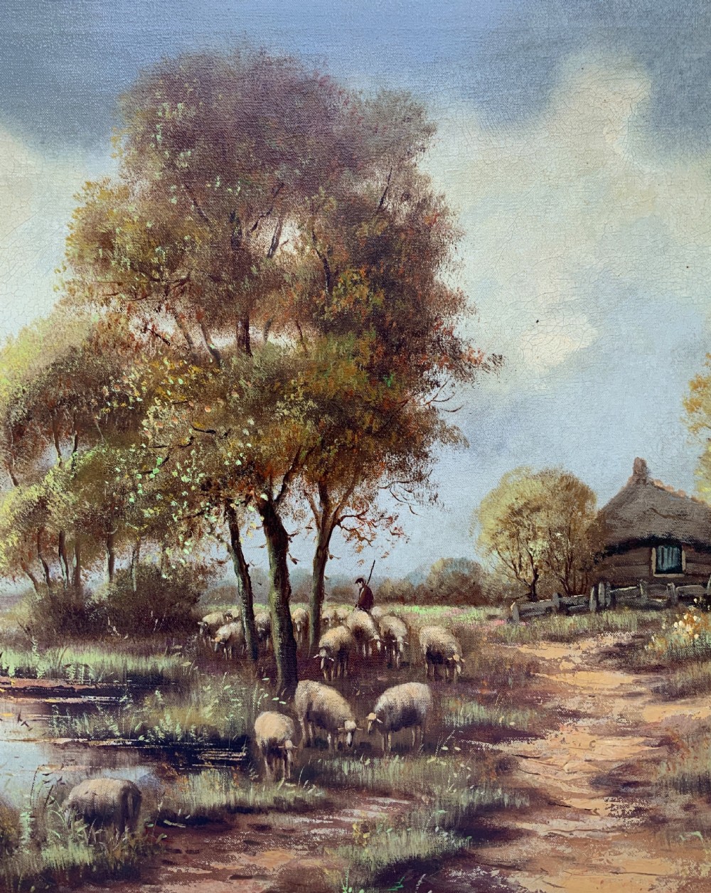 A framed oil painting on canvas depicting a rural autumn landscape with sheep grazing along a riverbank near a cottage under a cloudy sky. View V